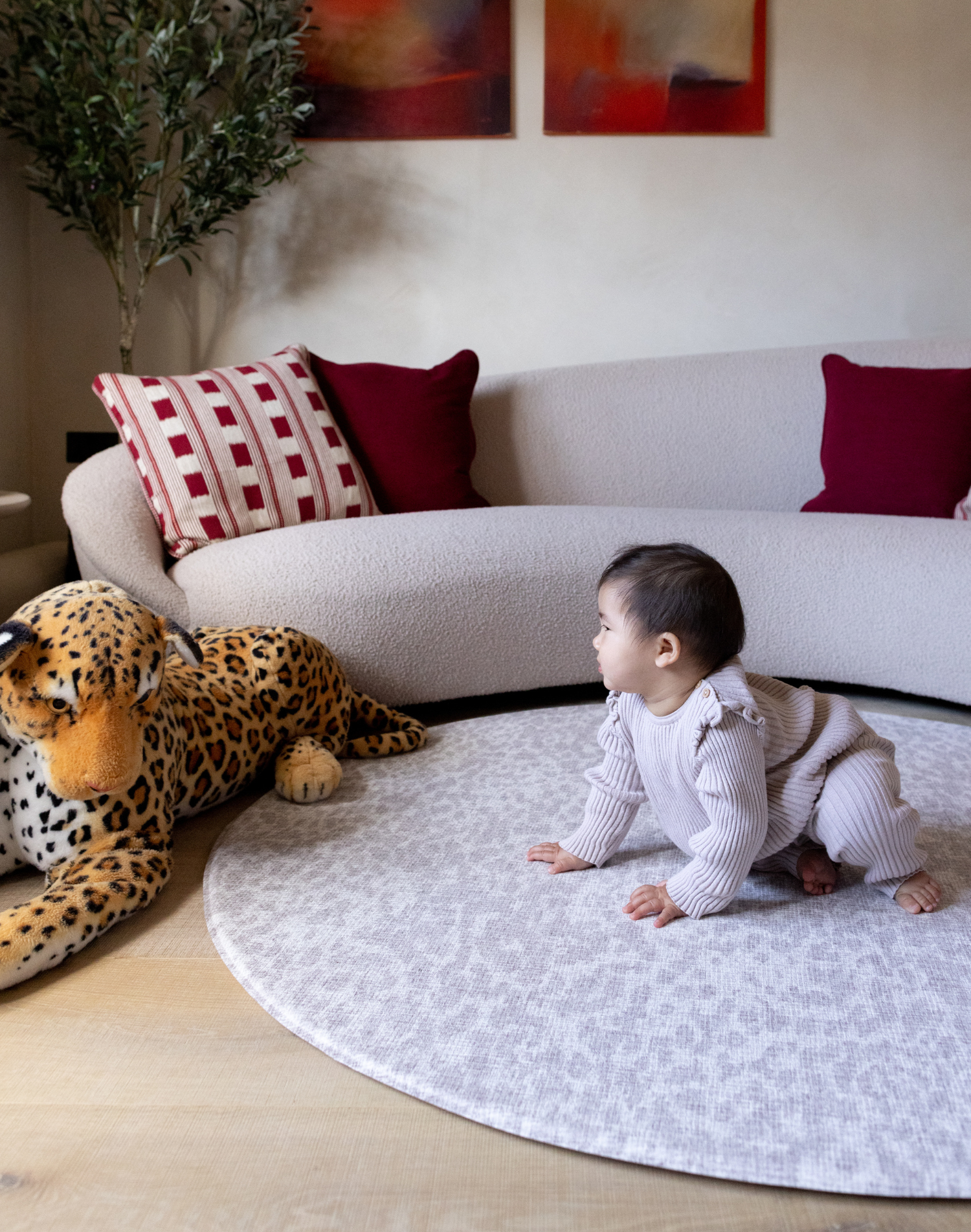 Baby crawls on grey leopard print playmat providing support on the floor during play time with a large soft leopard toy