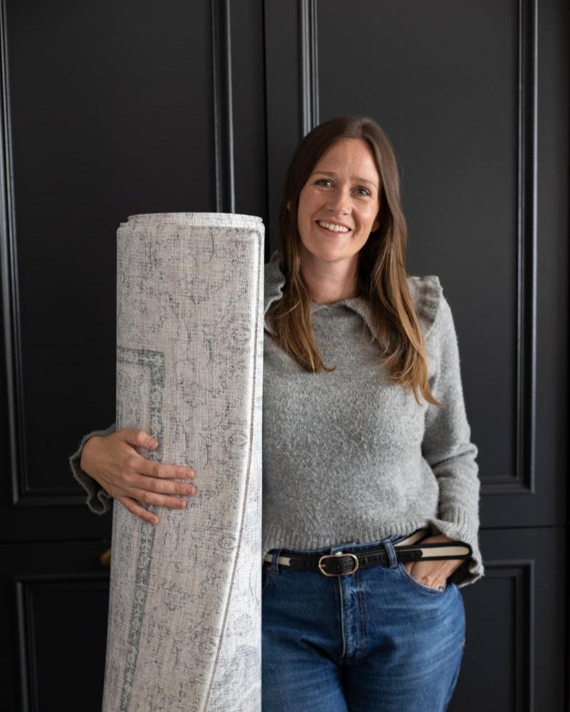 Susie Stubbs, founder of Totter + Tumble holding a large rolled grey playmat
