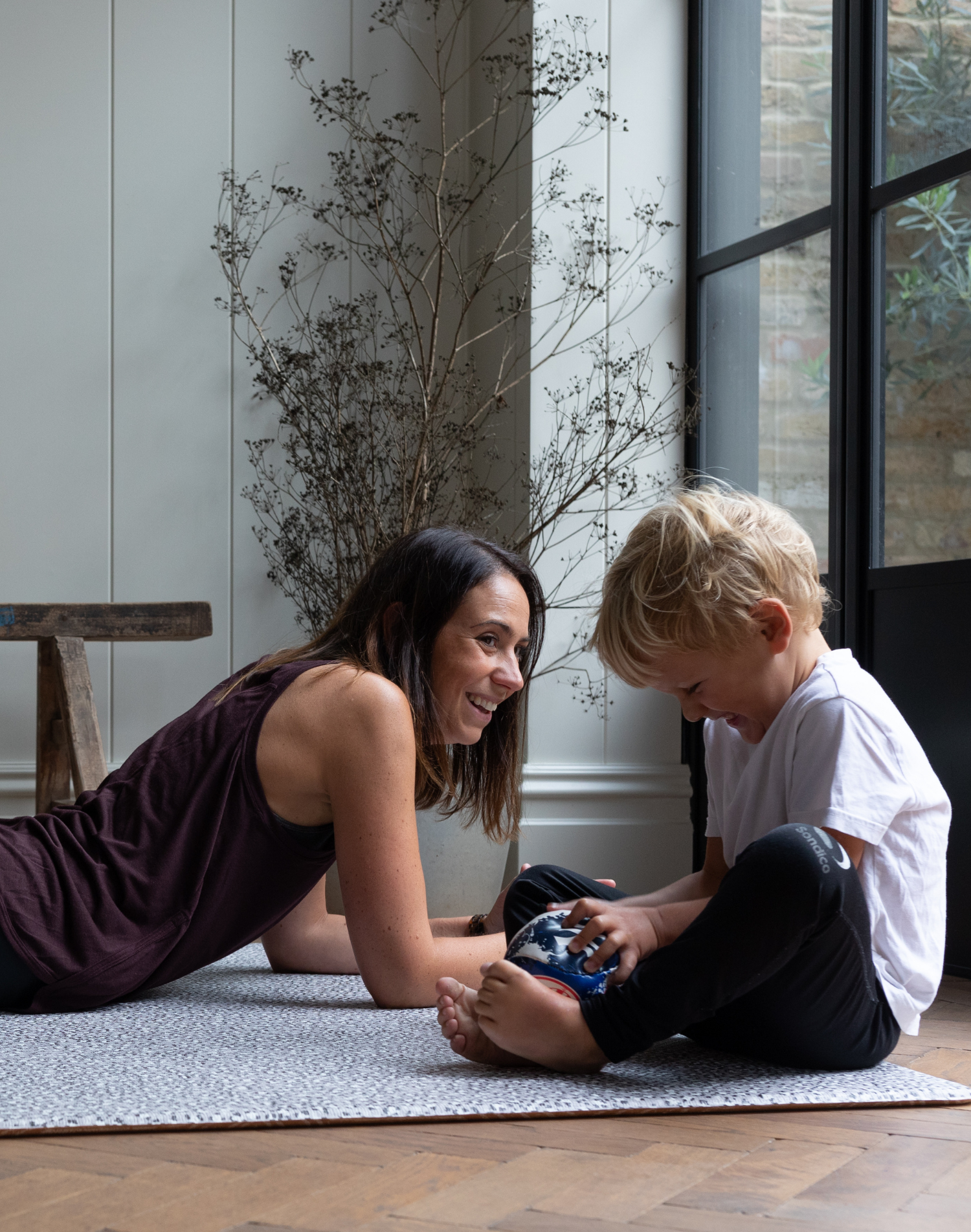 Exercising lady and boy giggle on the floor supported by leopard print playmat by totter and tumble