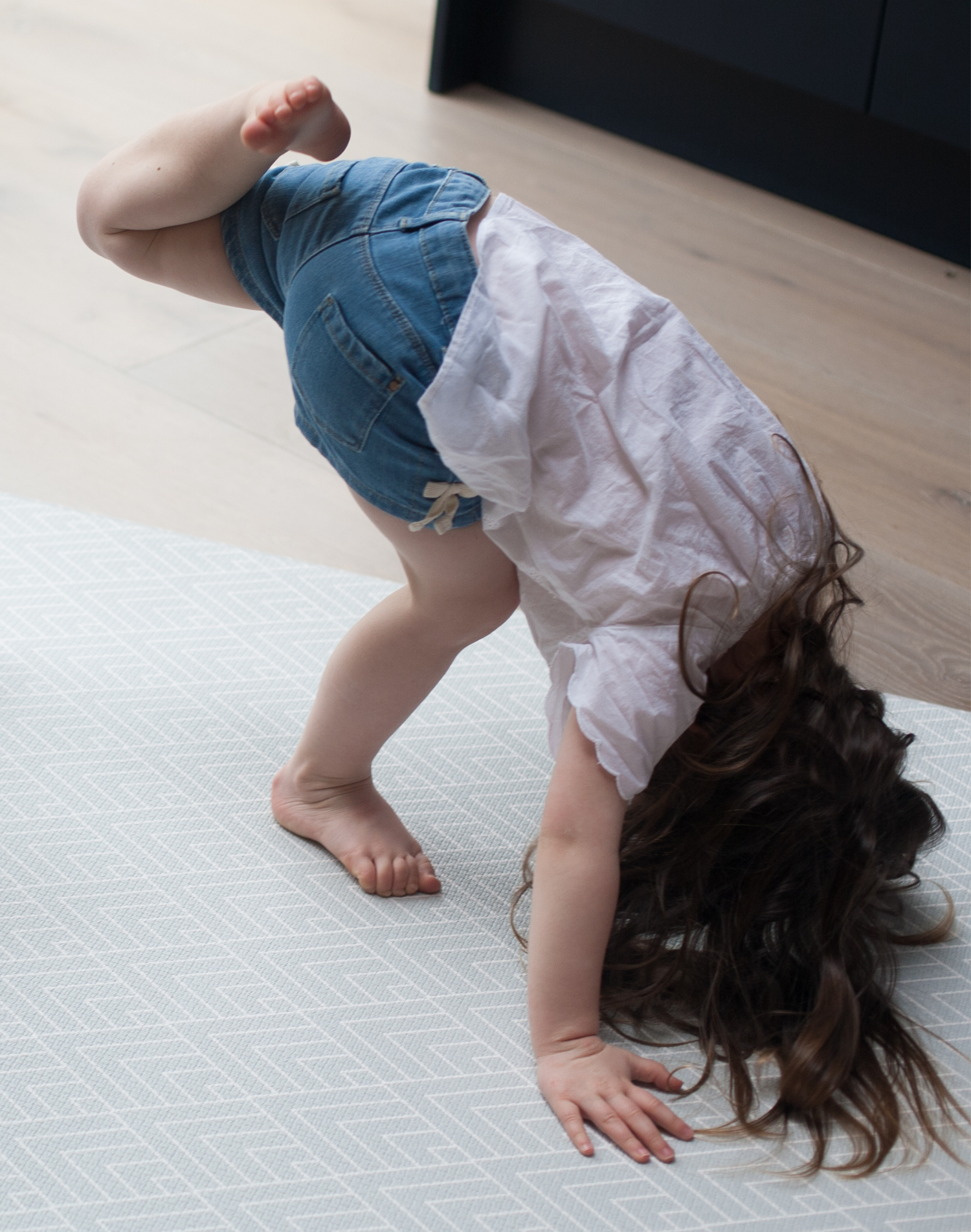 Little girl stretches out on mouldable playmat with thick luxury memory foam and a grey pattern