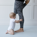 Little baby holds the legs of lady working out on the large grey exercise mat by totter and tumble