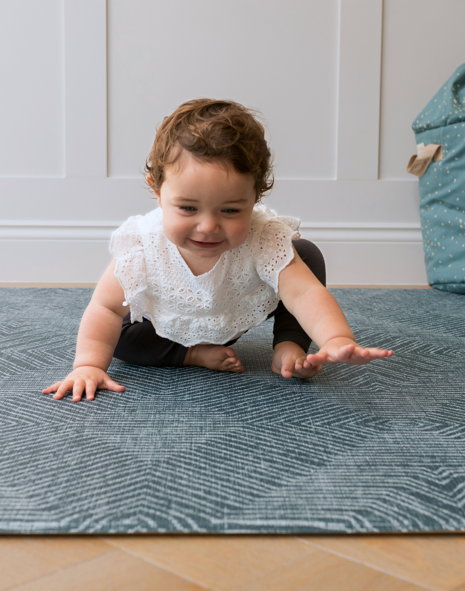Toddler sitting on teal Wanderlust play rug by Totter and tumble with thick foam to support floor play for the whole family