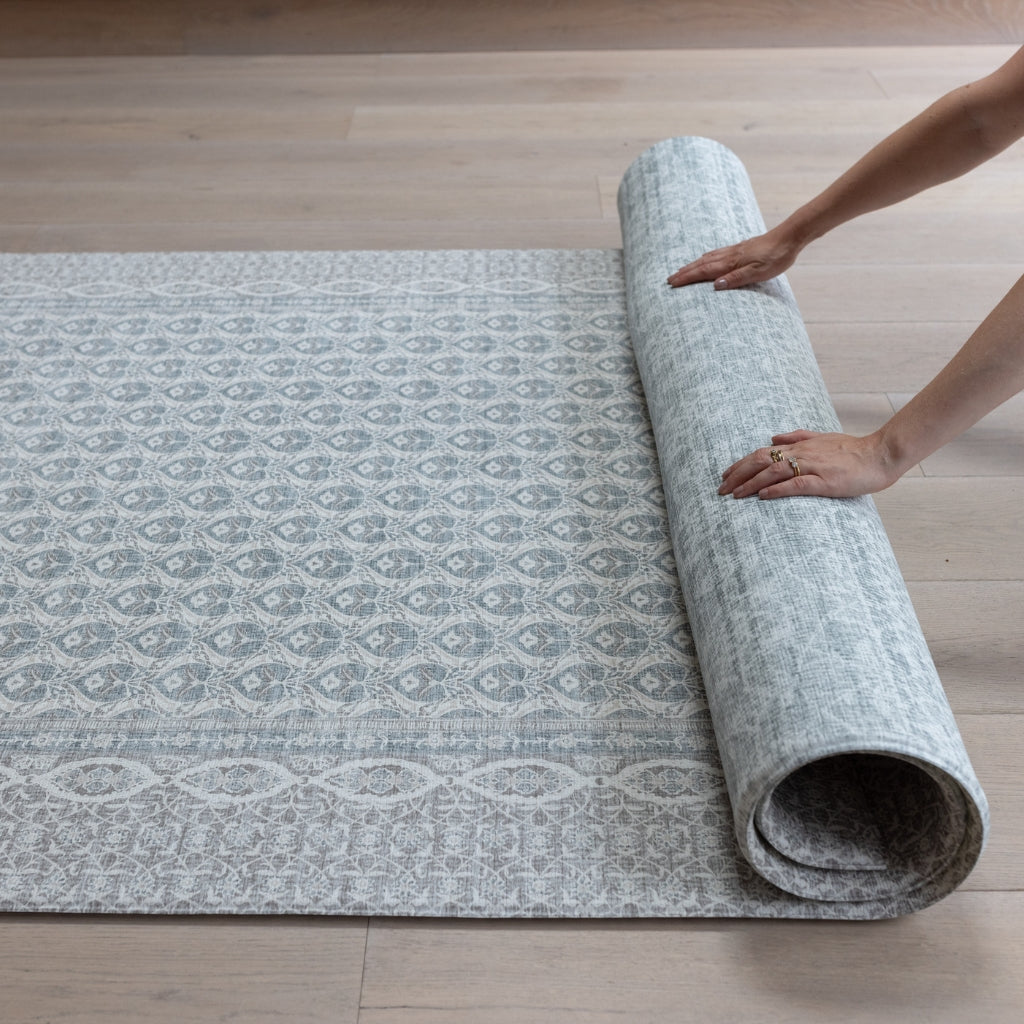 Hands roll up a large baby playmat with a hazy blue-grey medallion pattern  