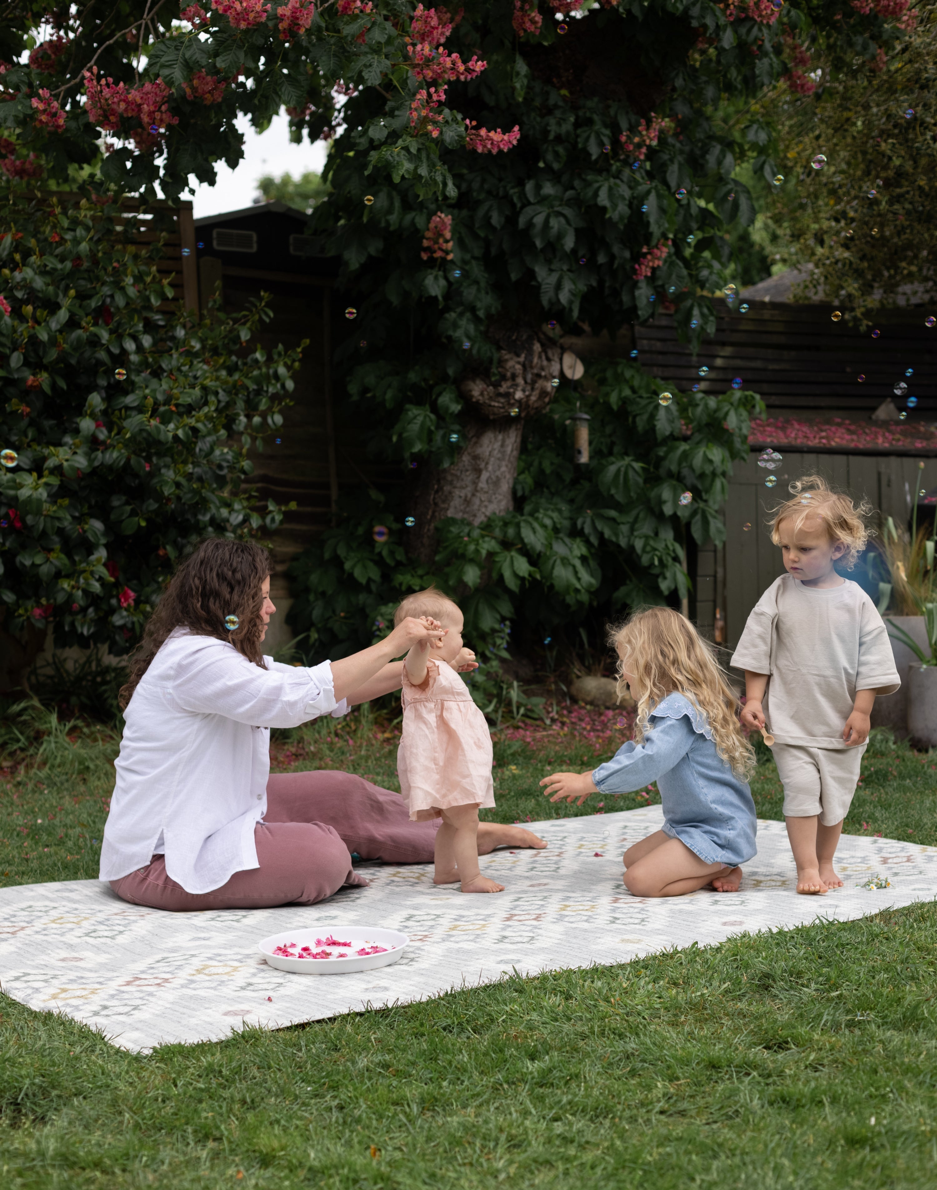 Woman and children playing outdoors on a totter and tumble playmat suitable for both indoors and outdoor use