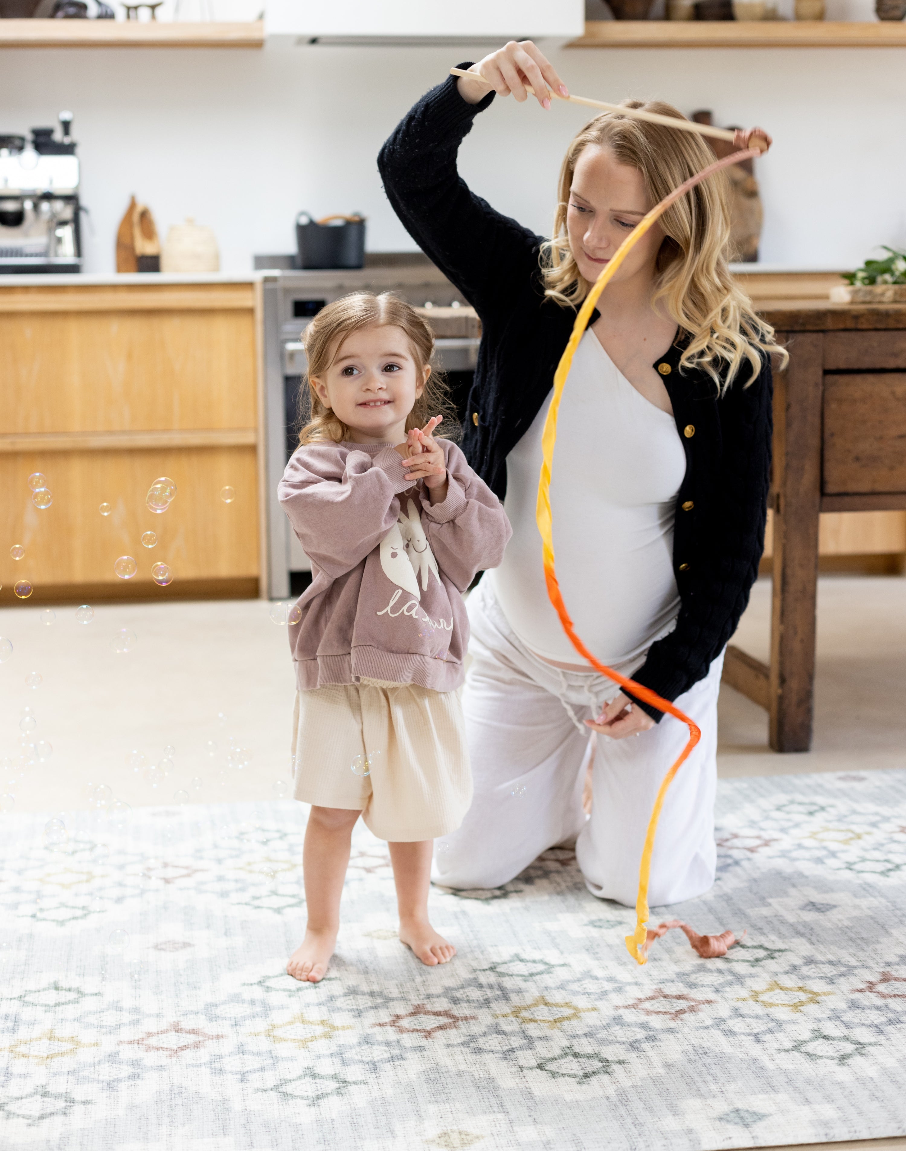 Pregnant mum playing with toddler on the floor knees on her totter and tumble playmat. 