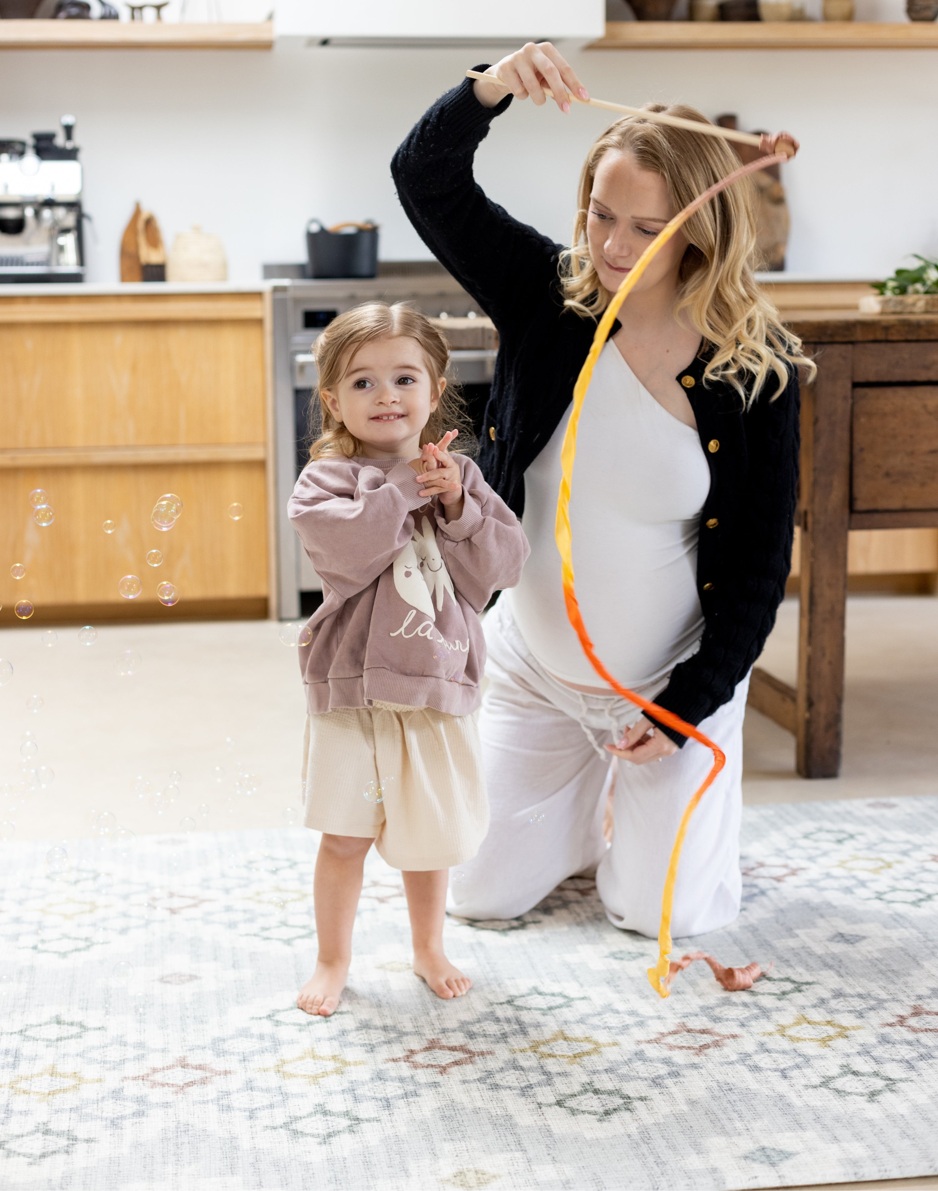 Pregnant mum playing with toddler on the floor knees on her totter and tumble playmat. 