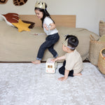 Two children playing on a bed with toys in a bedroom setting on a neutral totter and tumble playmat in a floral design easy to suit your home interior and support family life