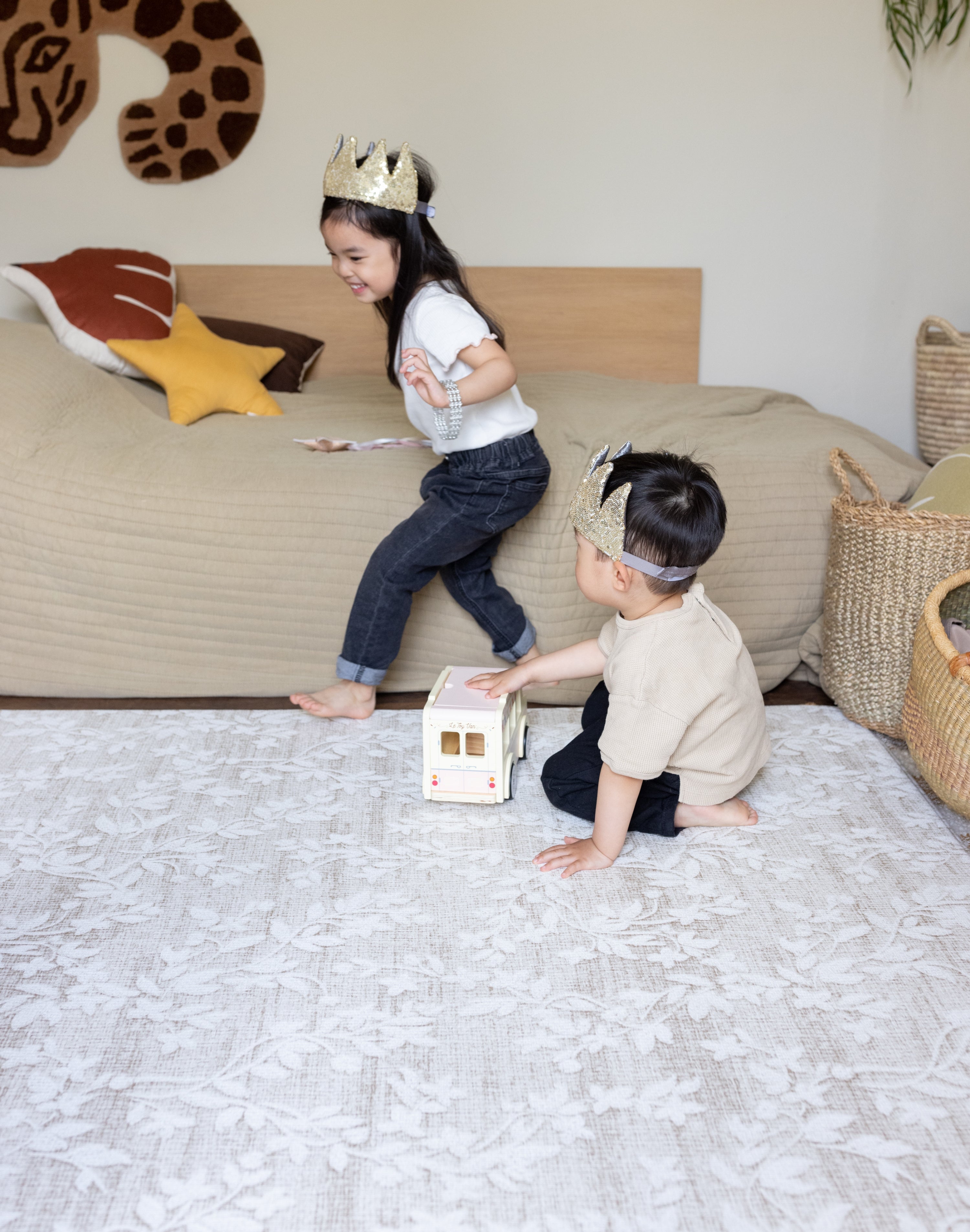 Two children playing on a bed with toys in a bedroom setting on a neutral totter and tumble playmat in a floral design easy to suit your home interior and support family life