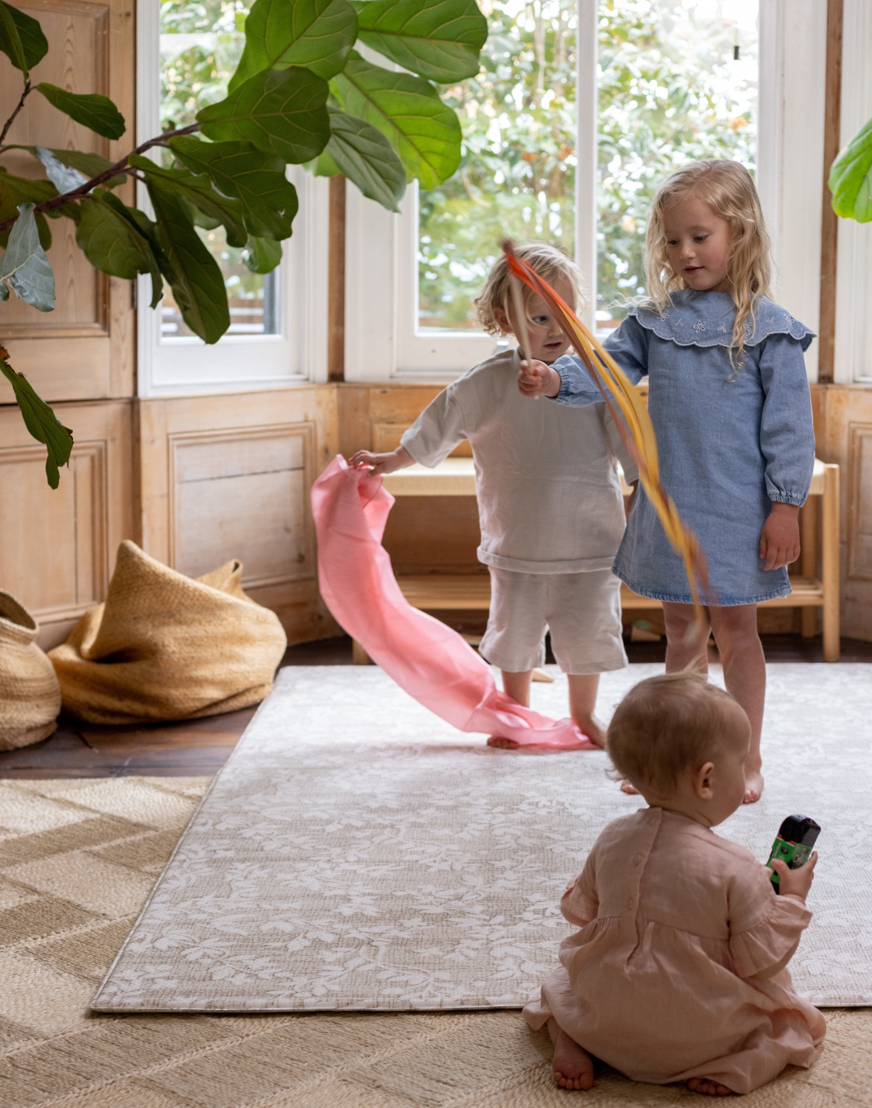 Three children playing with colorful ribbons in a home setting on the extra large totter and tumble one piece playmat