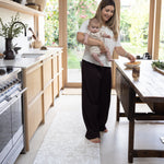 Woman holding a baby in a modern kitchen whilst standing on a play runner from totter and tumble
