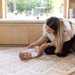 Mum playing with a baby on a patterned padded playmat from Totter + Tumble in a sunlit room.