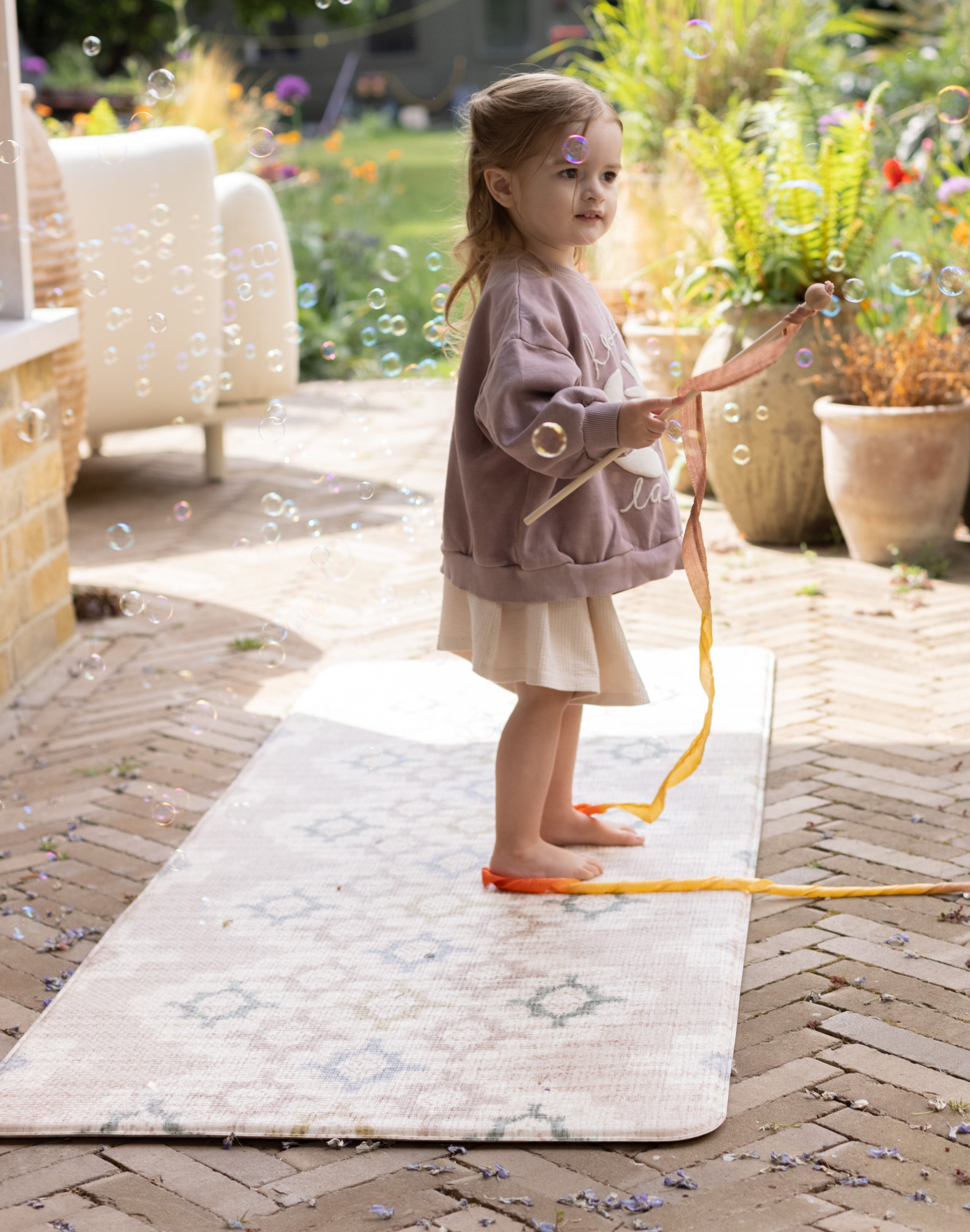 Little girl playing with a wand on a totter and tumble play runner suitable to use outside or indoors