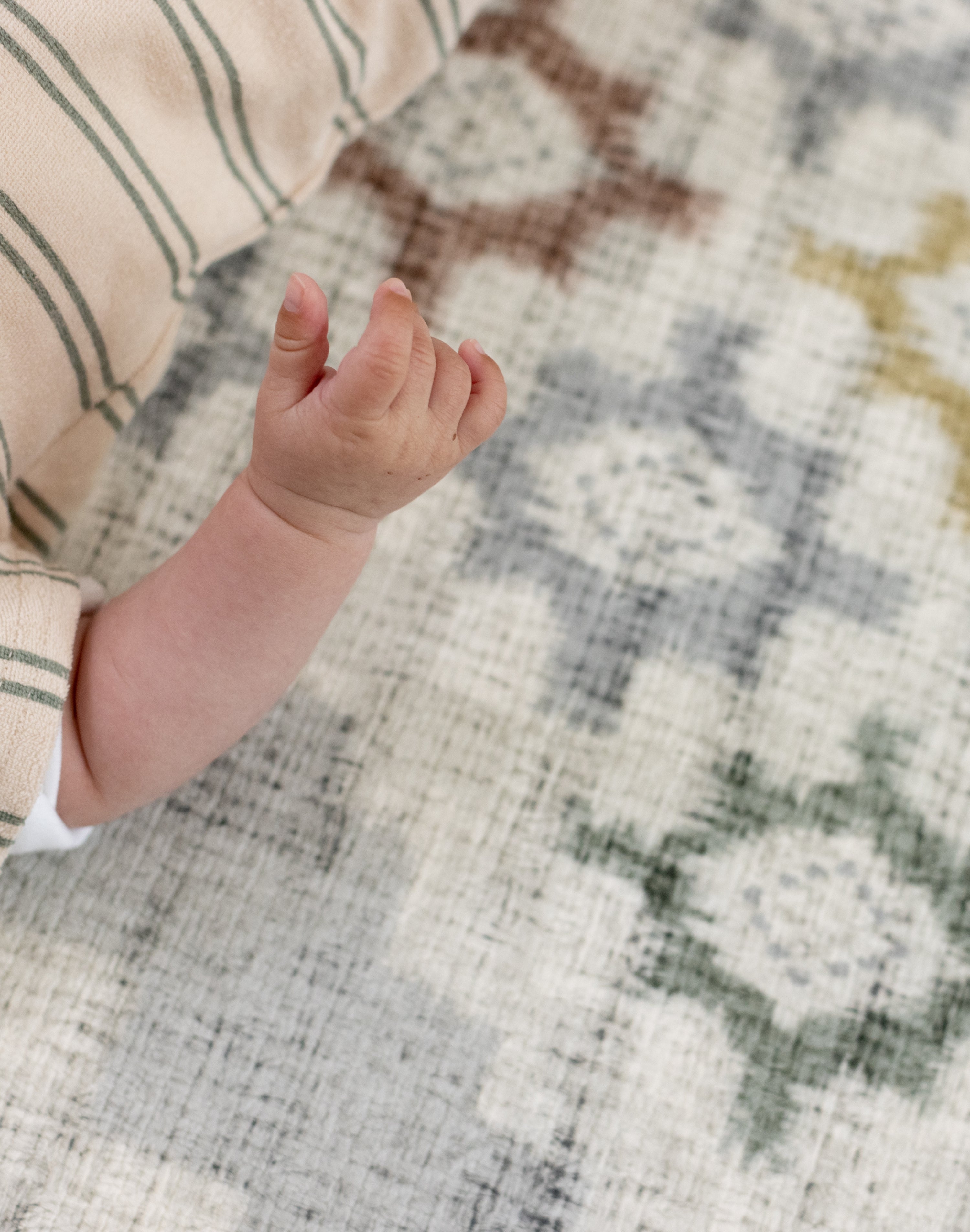 Close-up of a baby's hand on an area rug equivalent called totter and tumble play mat 