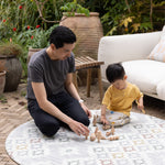 Father and son playing with wooden toys on a round, play mat from Totter and Tumble on patio outdoors. 