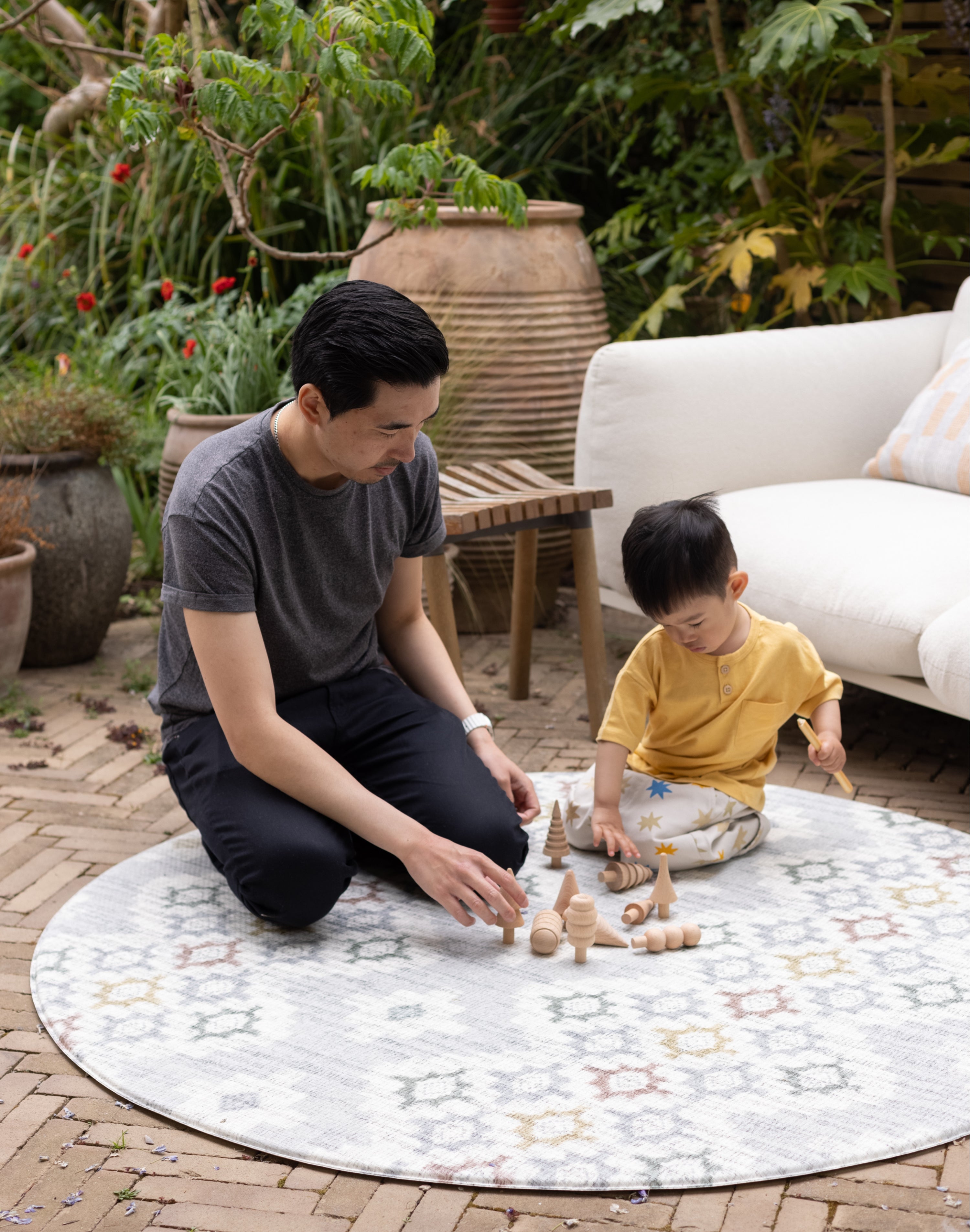 Father and son playing with wooden toys on a round, play mat from Totter and Tumble on patio outdoors. 