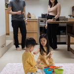 Family of four in a kitchen with children playing on the floor mat.