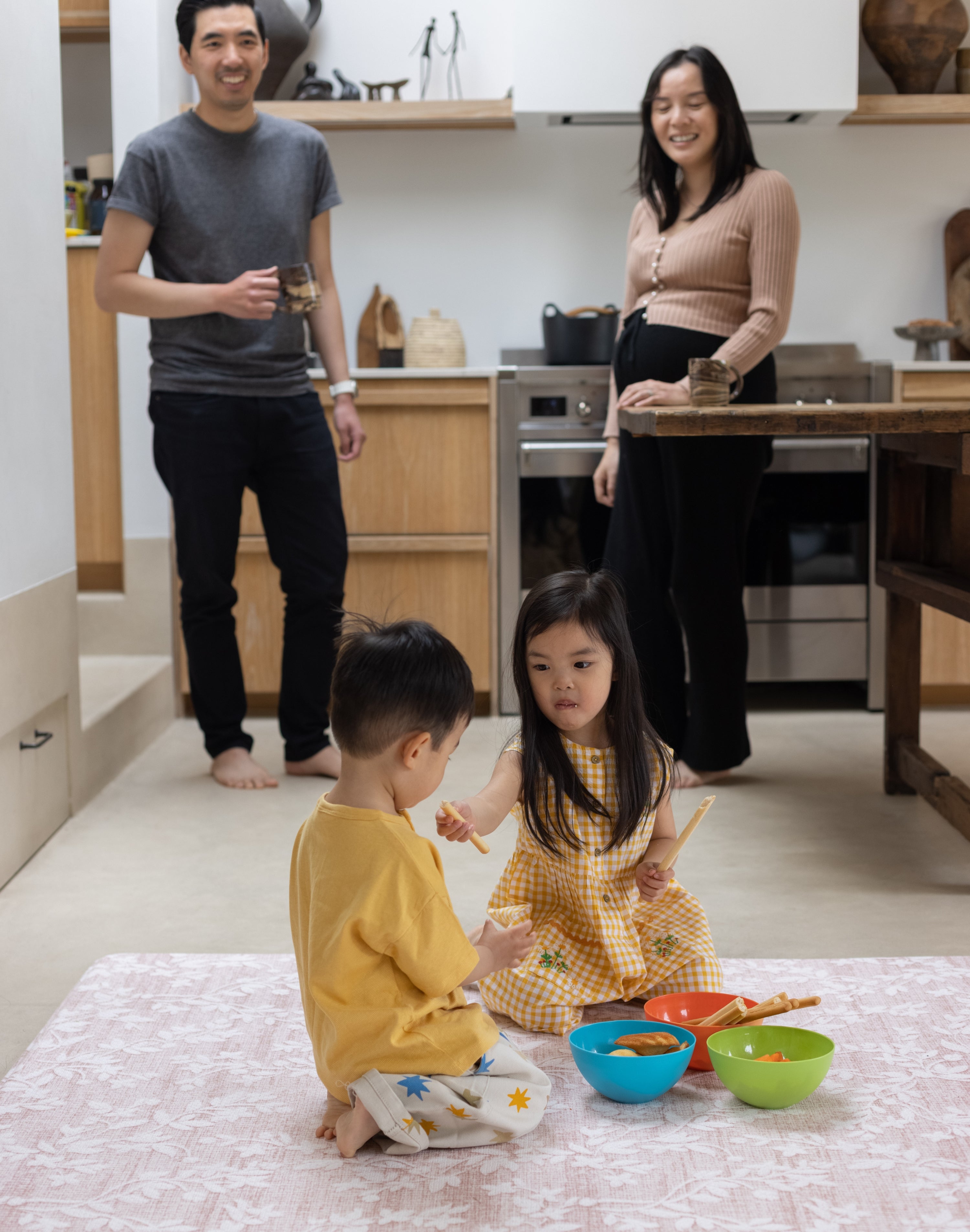 Family of four in a kitchen with children playing on the floor mat.