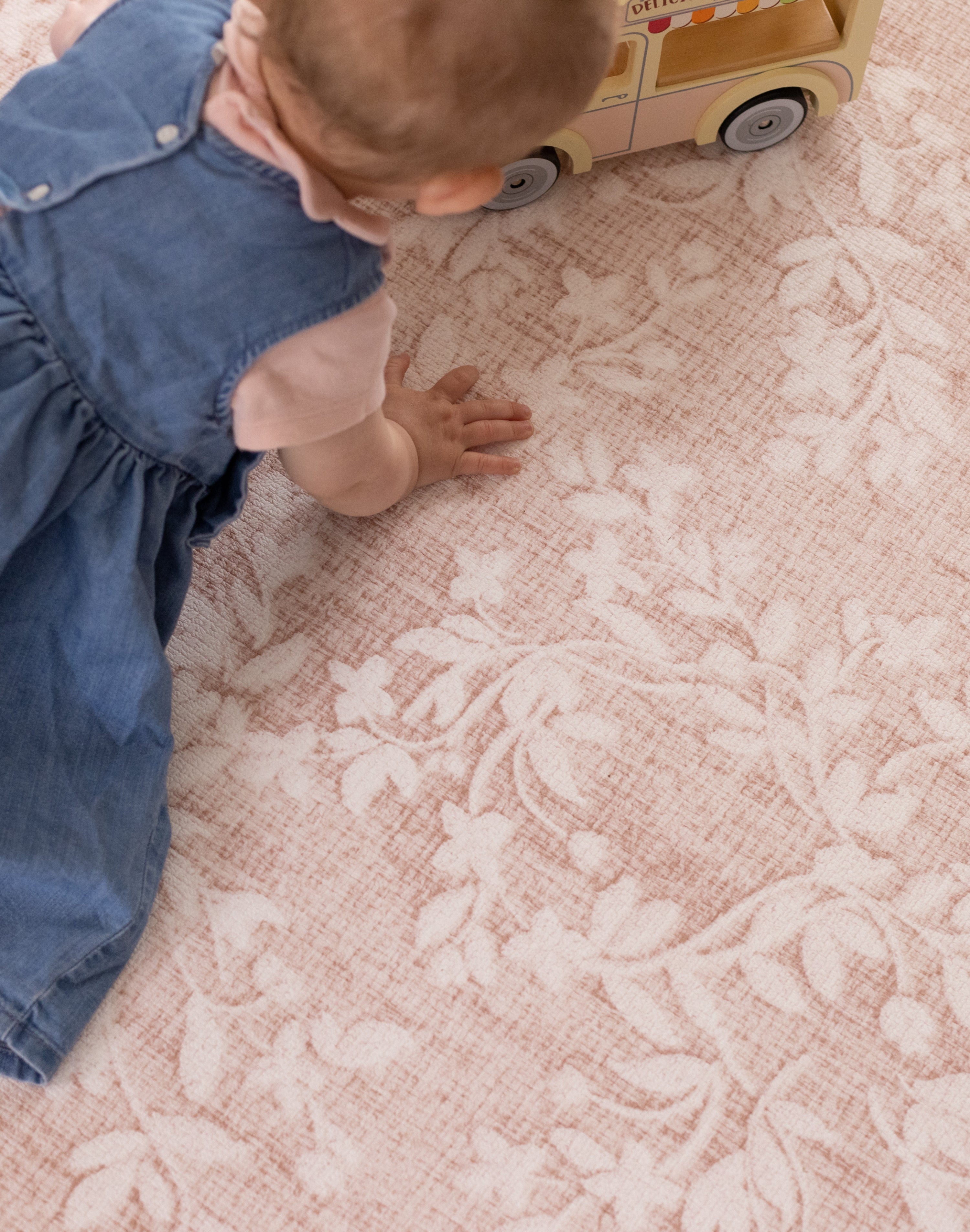 Child in a blue dress playing with a toy car on a floral print playmat design in pink - alternative to rug or carpet