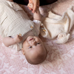 Baby lying on a pink blanket with a person holding their hand, totter and tumble playmats are safe from birth