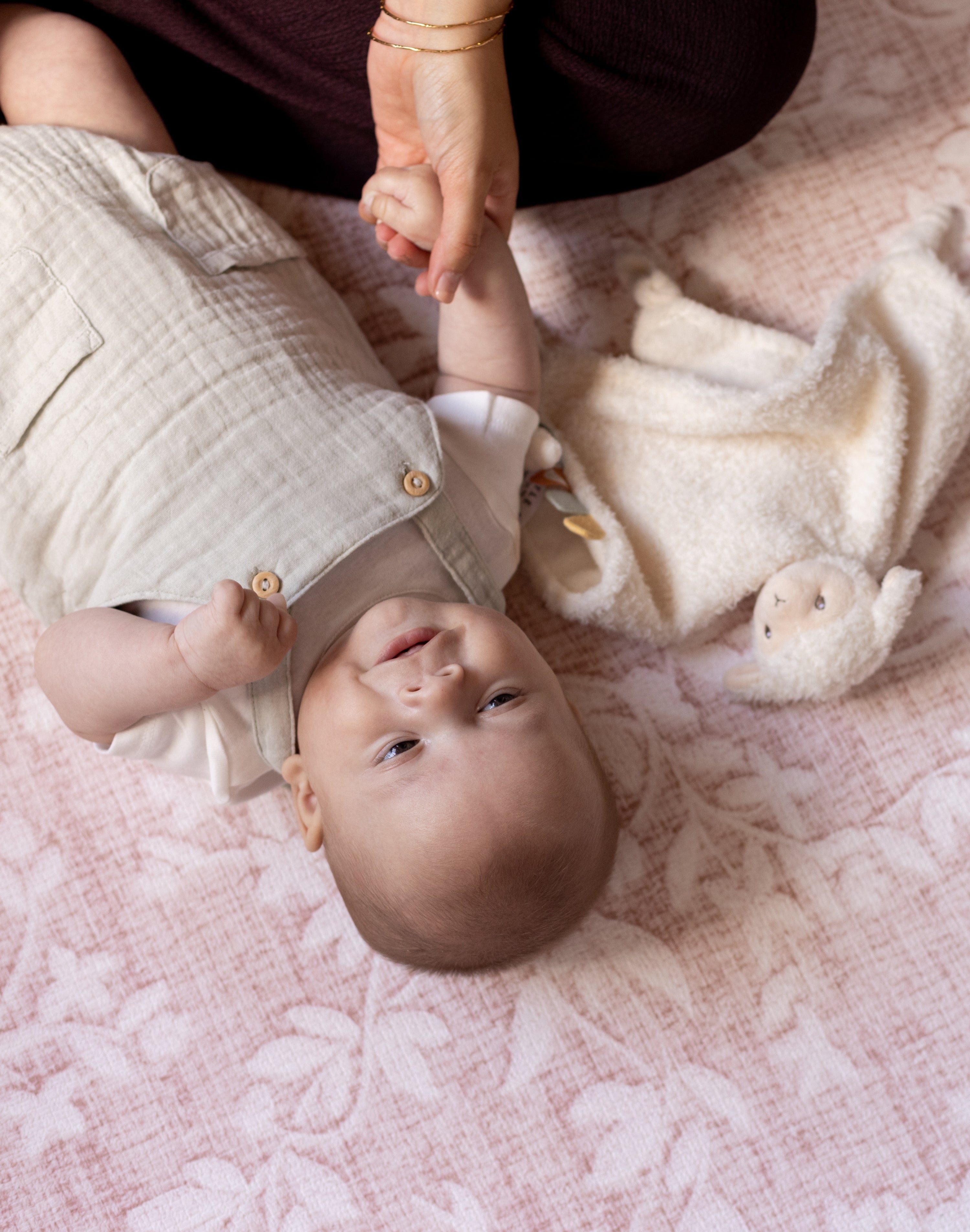 Baby lying on a pink blanket with a person holding their hand, totter and tumble playmats are safe from birth