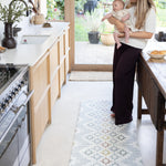 Mum holding newborn in the kitchen standing on top of play runner kitchen standing mat. 