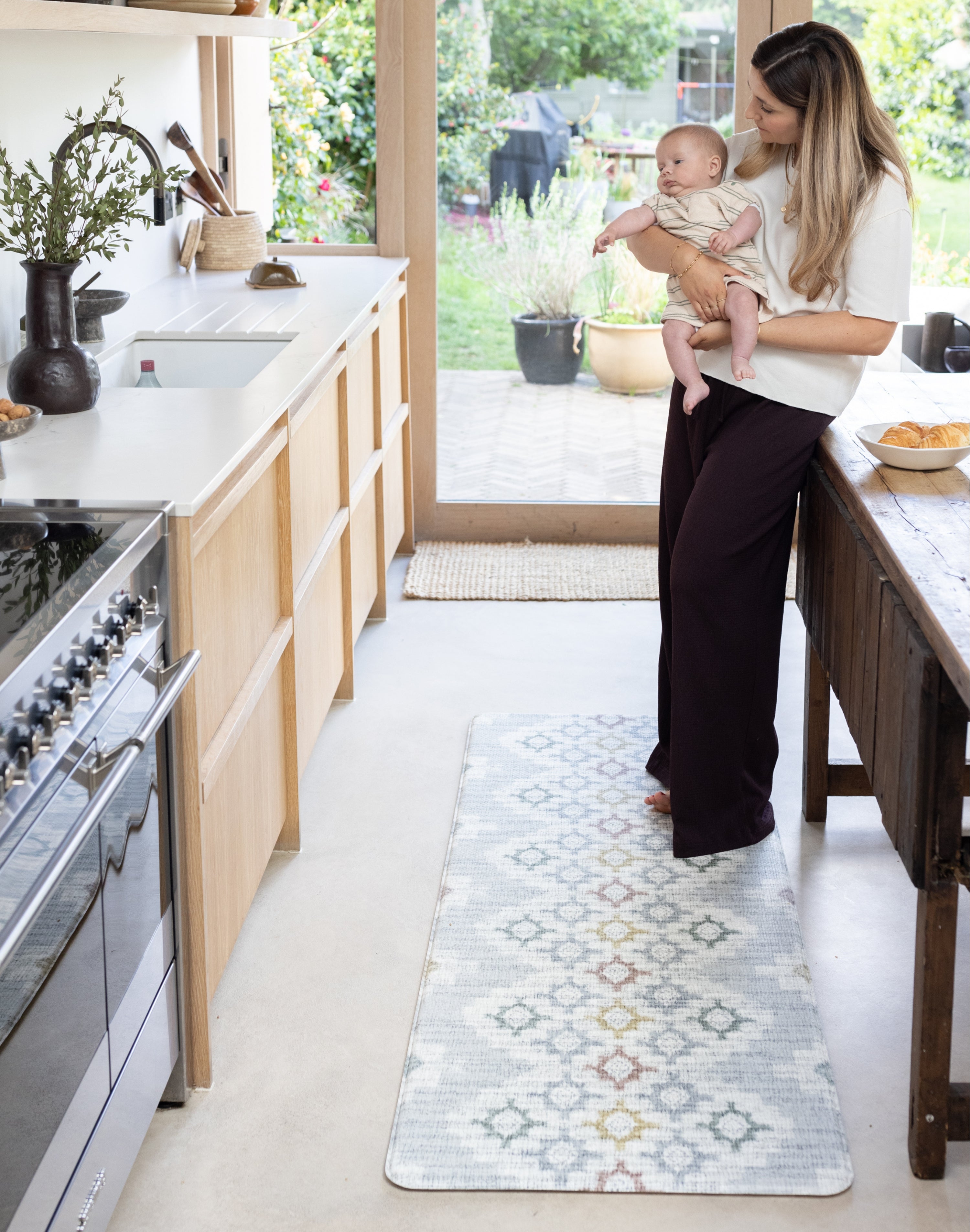Mum holding newborn in the kitchen standing on top of play runner kitchen standing mat. 