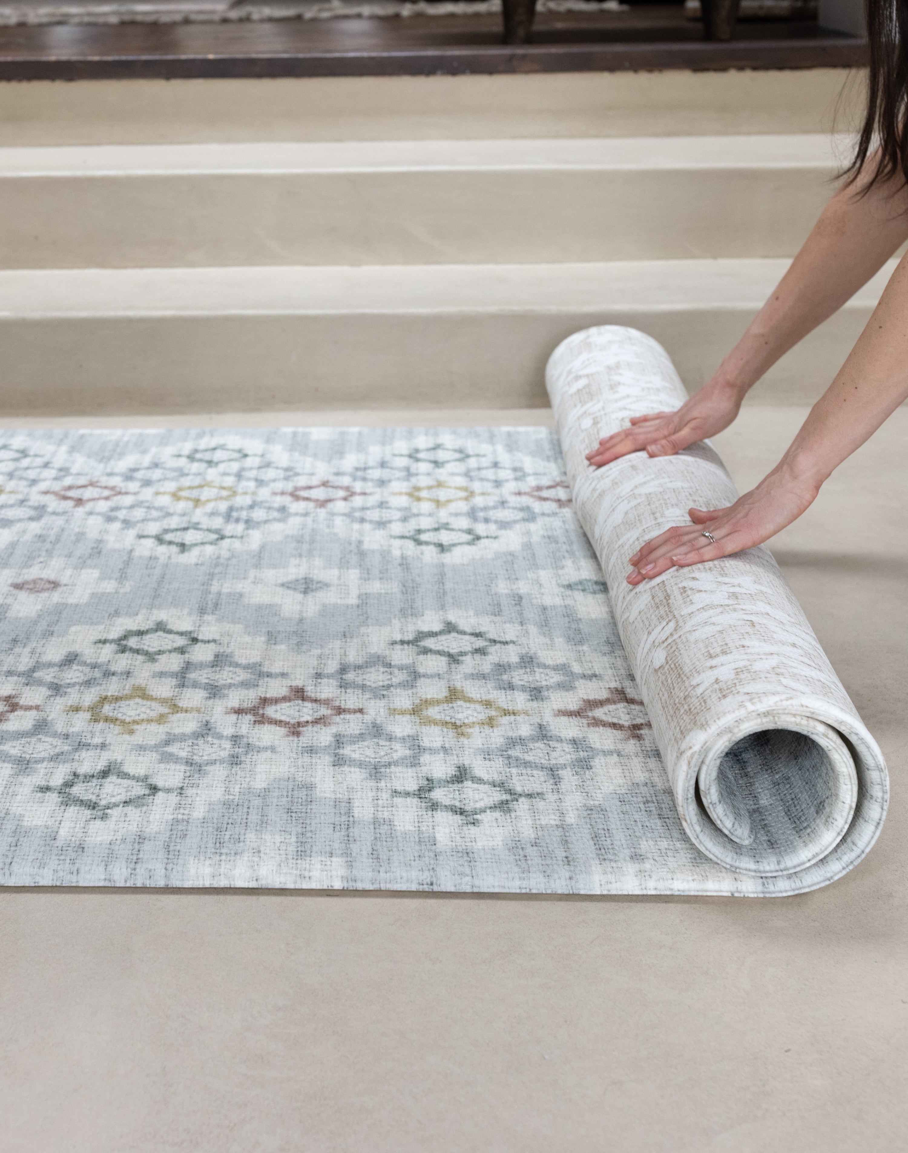 Person unrolling a patterned rug on a floor