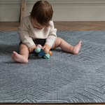 Little baby sits supported on the modern play mat by totter and tumble with a rug like design in dark charcoal made for modern homes 