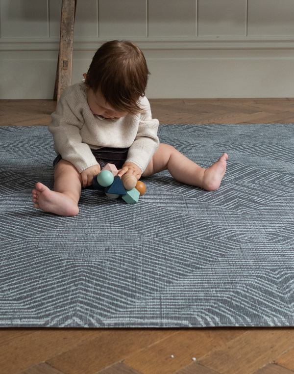 Little baby sits supported on the modern play mat by totter and tumble with a rug like design in dark charcoal made for modern homes 