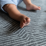 Little feet rest supported on the luxury memory foam mat by totter and tumble with a monochrome rug like design