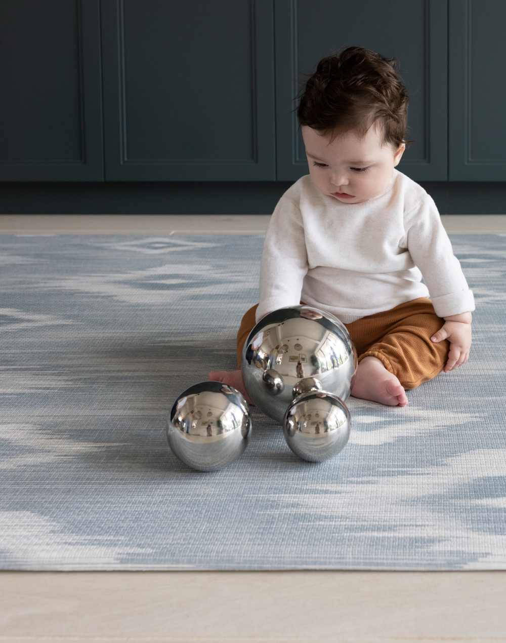 Baby playing with sensory balls on Light blue and beige play mat with subtle diamond design inspired by ikat motifs ideal for family living spaces