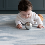 Baby playing with sensory ball on Playroom mats by Totter and Tumble in stylish designs The Atlas has a beautiful ikat design in natural tones of blue and beige 