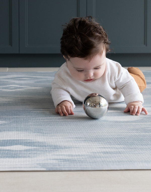Baby playing with sensory ball on Playroom mats by Totter and Tumble in stylish designs The Atlas has a beautiful ikat design in natural tones of blue and beige 