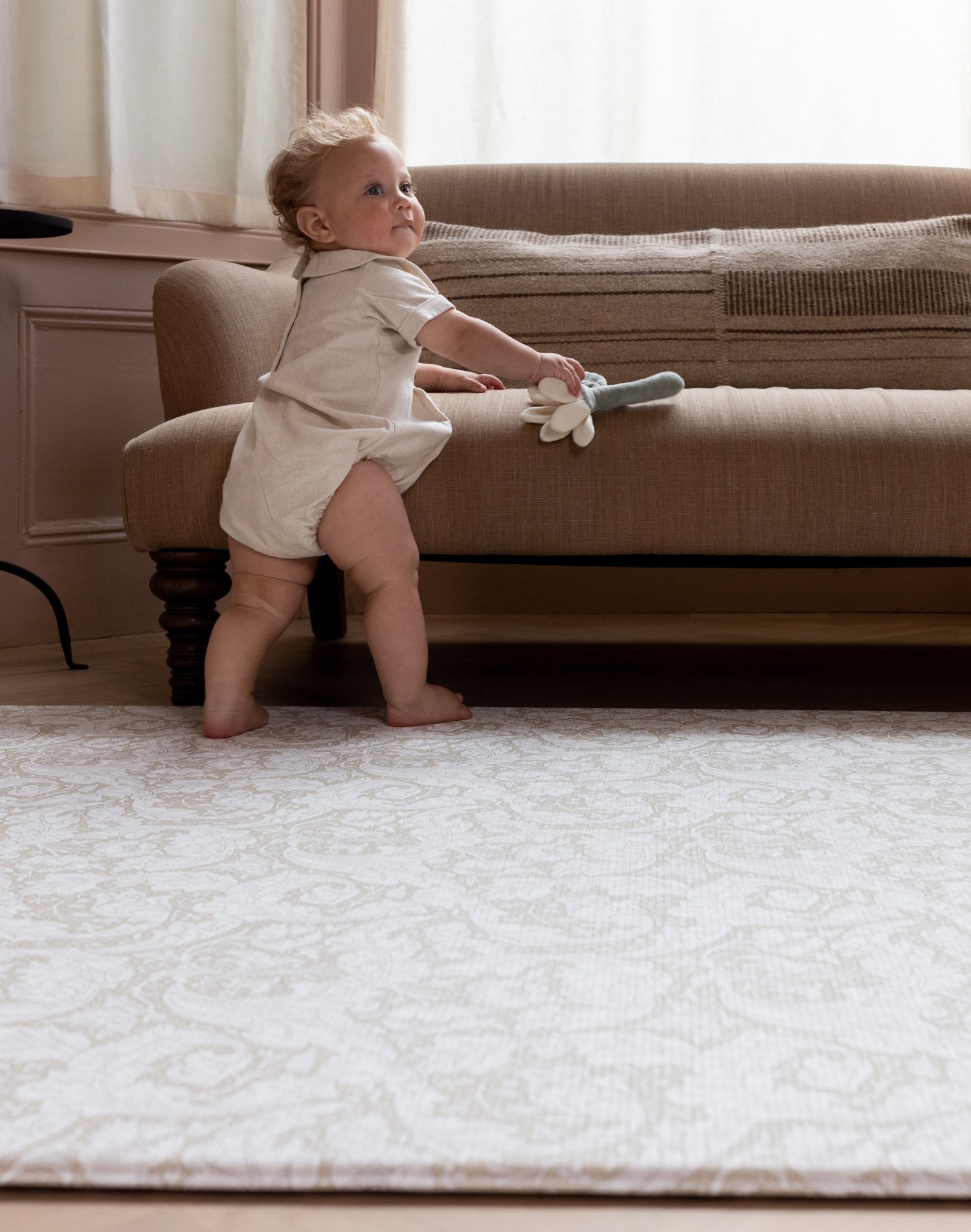 baby pulling up on sofa to standing on large padded playmat