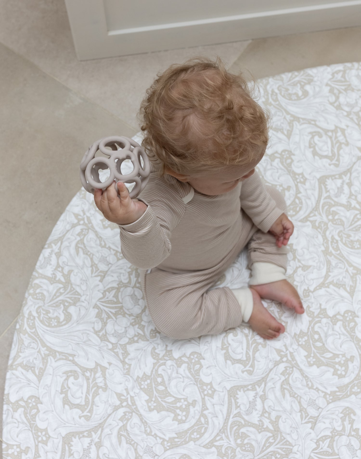 baby sitting on round neutral foam playmat with William Morris Bachelors Button design