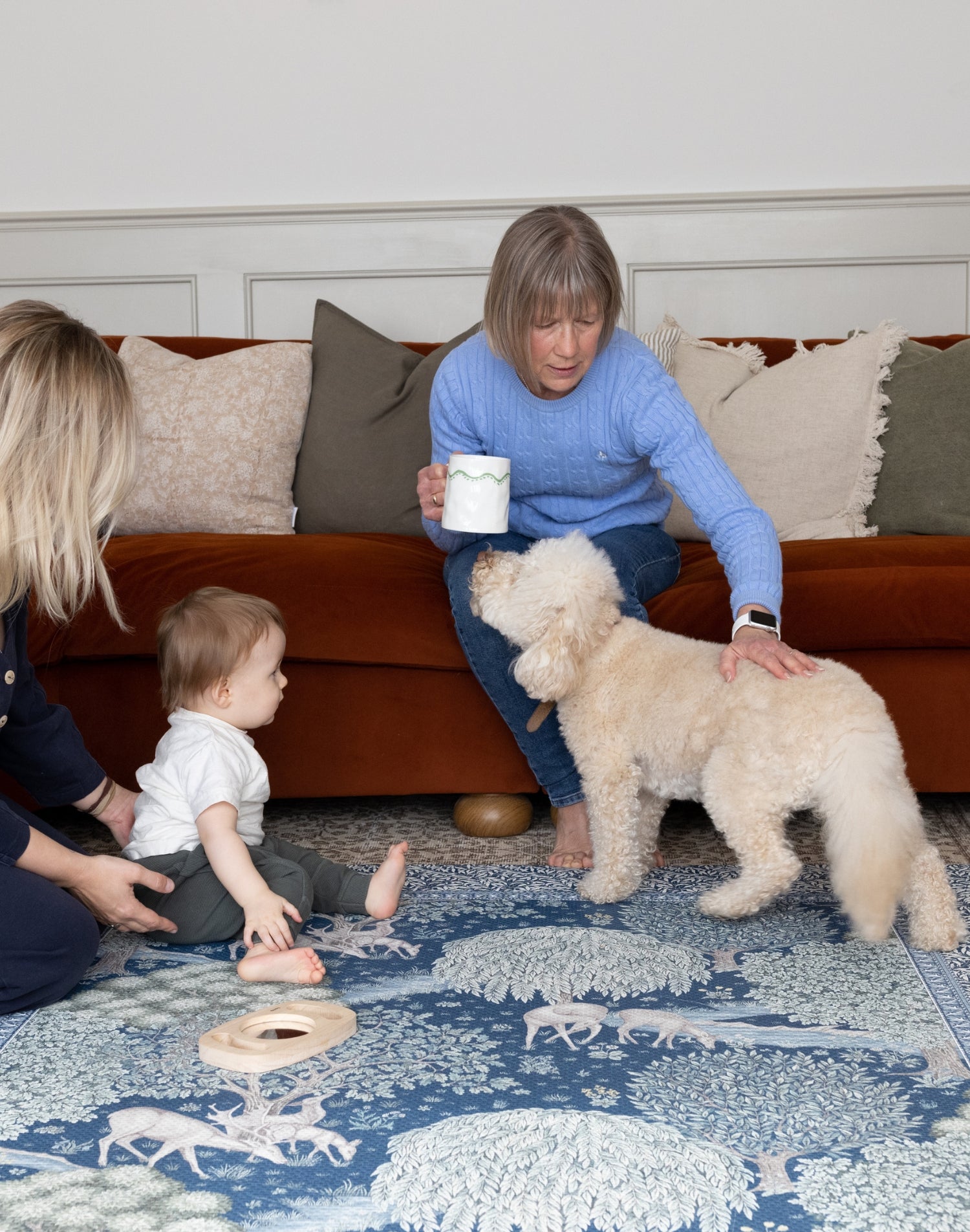 Stylish family setting with baby, mum, grandma and dog playing on a Totter + Tumble luxury playmat - a family-friendly interior essential with a two-sided luxury design.