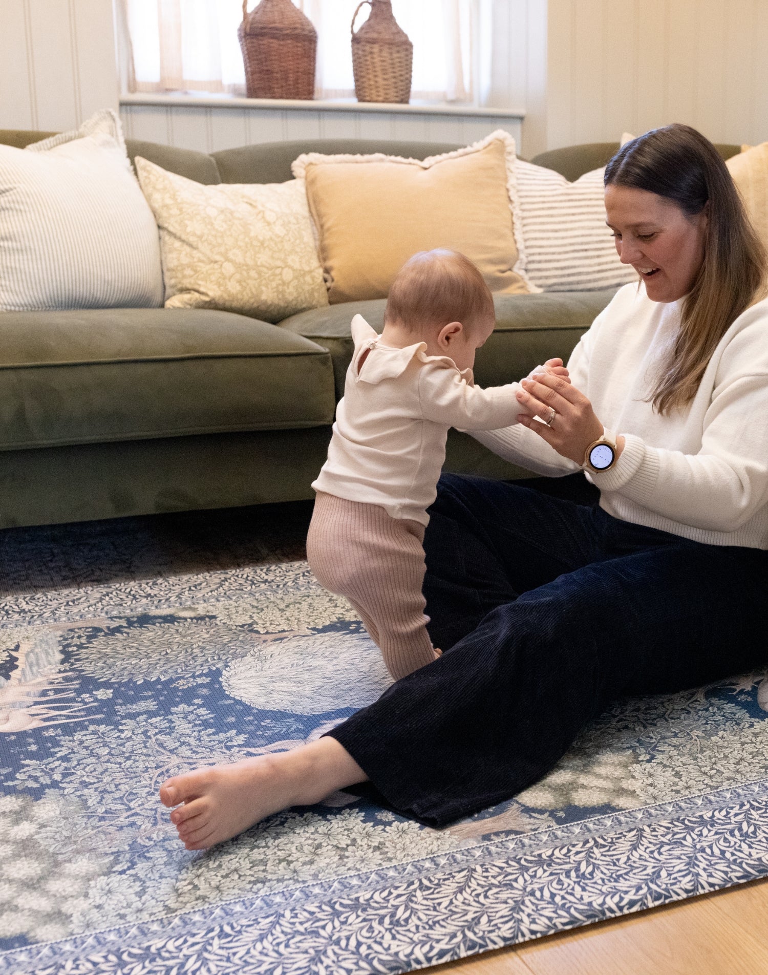 Parent supports standing baby on a luxury nursery play mat in warm woodland hues - a timeless, practical yet stylish baby product.