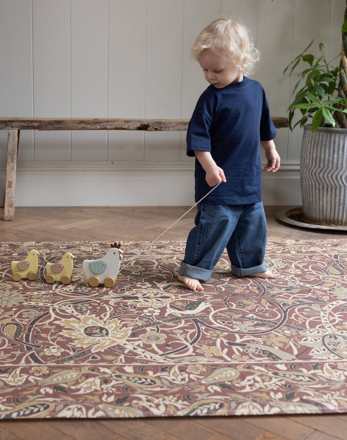 Child playing with toy ducks on a Persian patterned closed cell rug in a room with a wooden bench and plant.