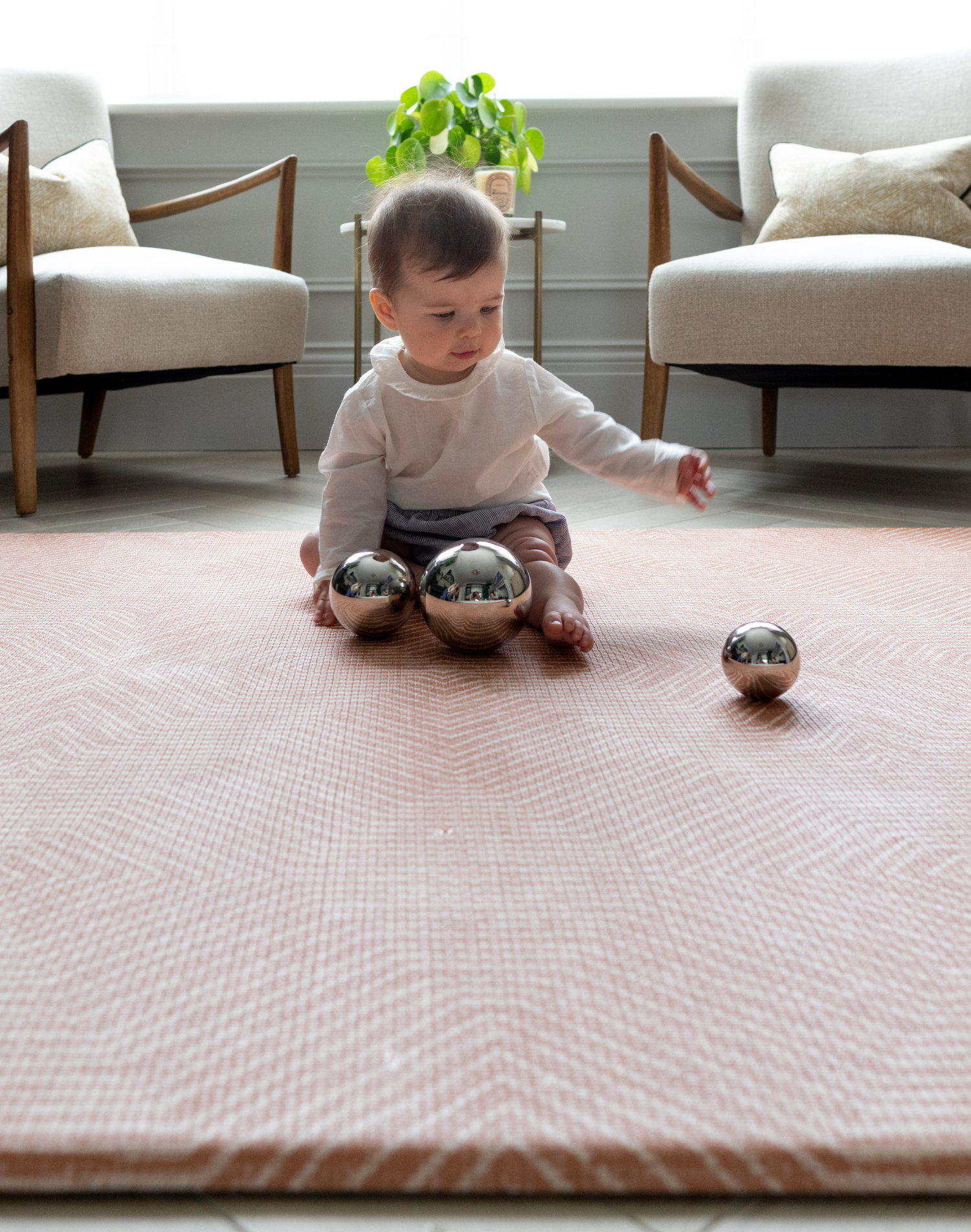 Baby girl enjoys sensory play time with metallic spheres sitting protected on a foam baby mat