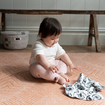 Baby reaches for sensory muslin supported on kids playmat with a warm terracotta kilim pattern 