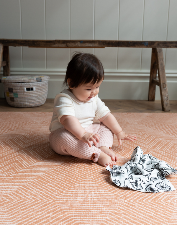 Baby reaches for sensory muslin supported on kids playmat with a warm terracotta kilim pattern 