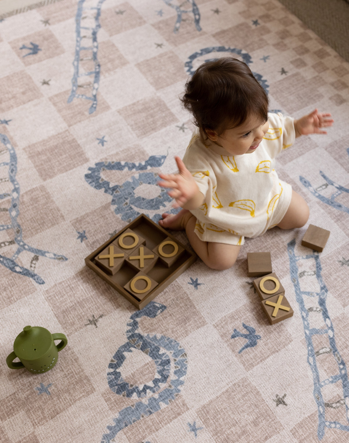 Baby sitting and playing on a neutral-toned luxury one-piece playmat with soft illustrated details in a light-filled home
