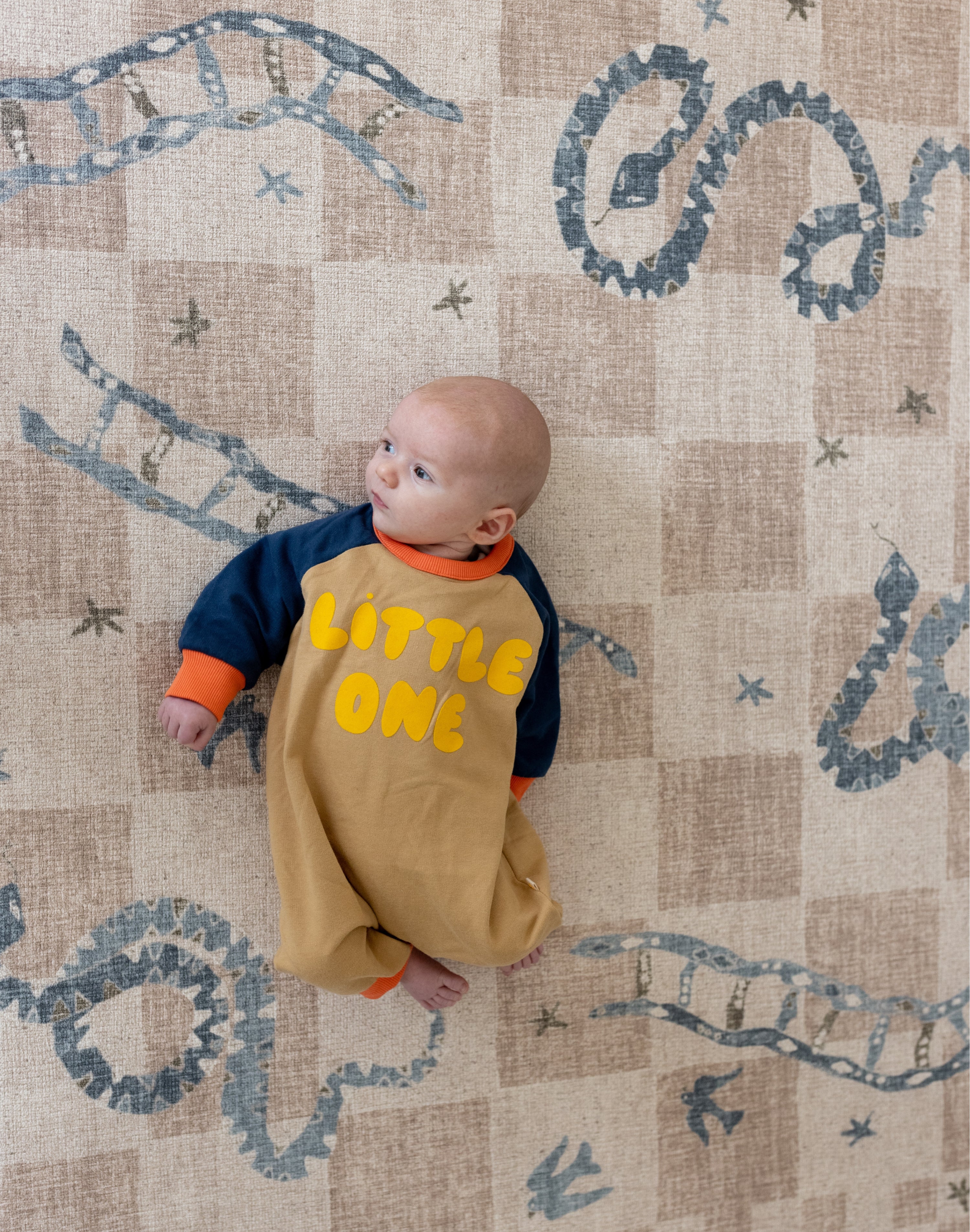 Infant lying comfortably on a padded luxury playmat with muted artwork designed for modern interiors
