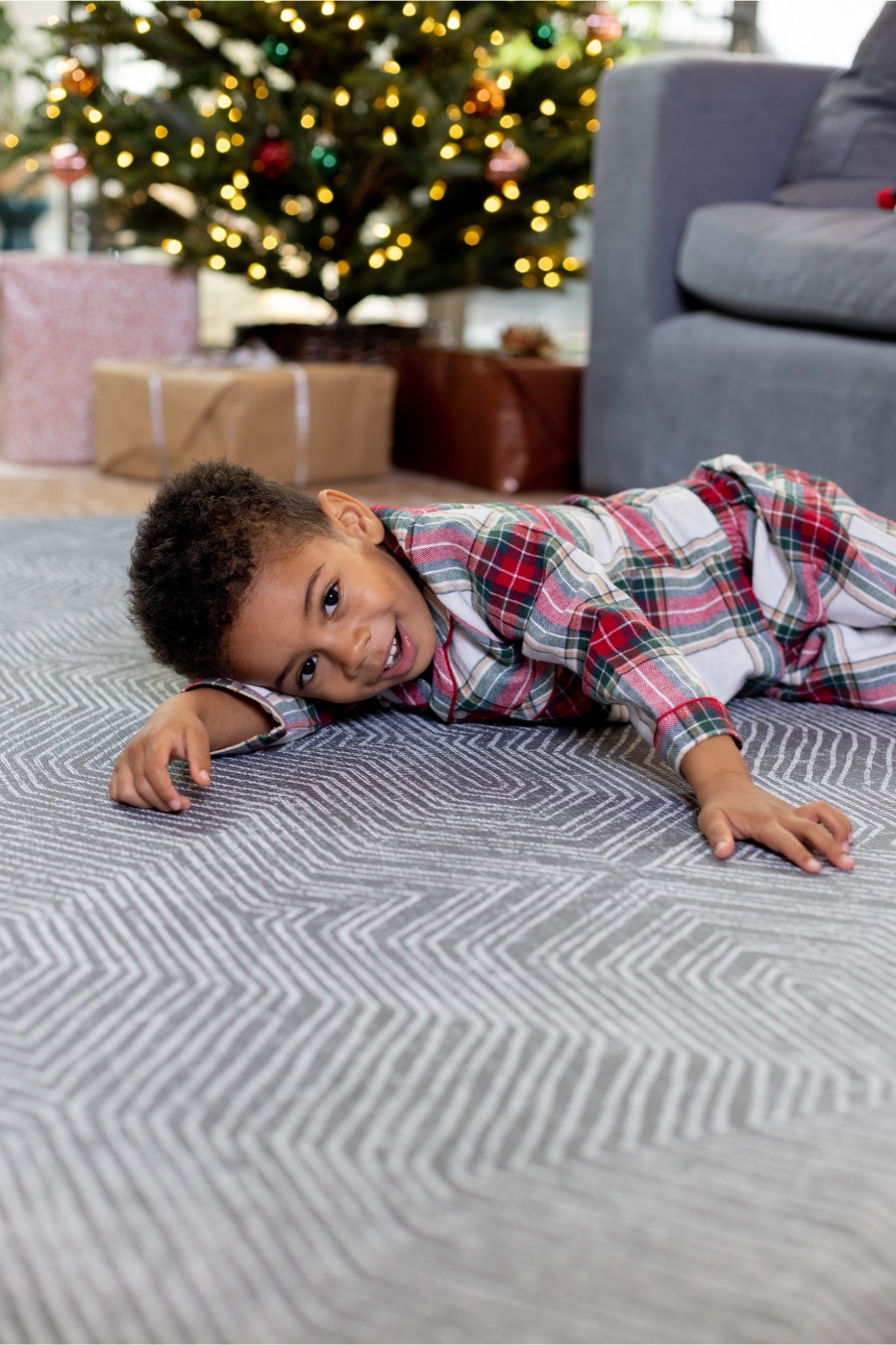 Child lying near the Christmas tree on a playmat, wearing Christmas pyjamas 