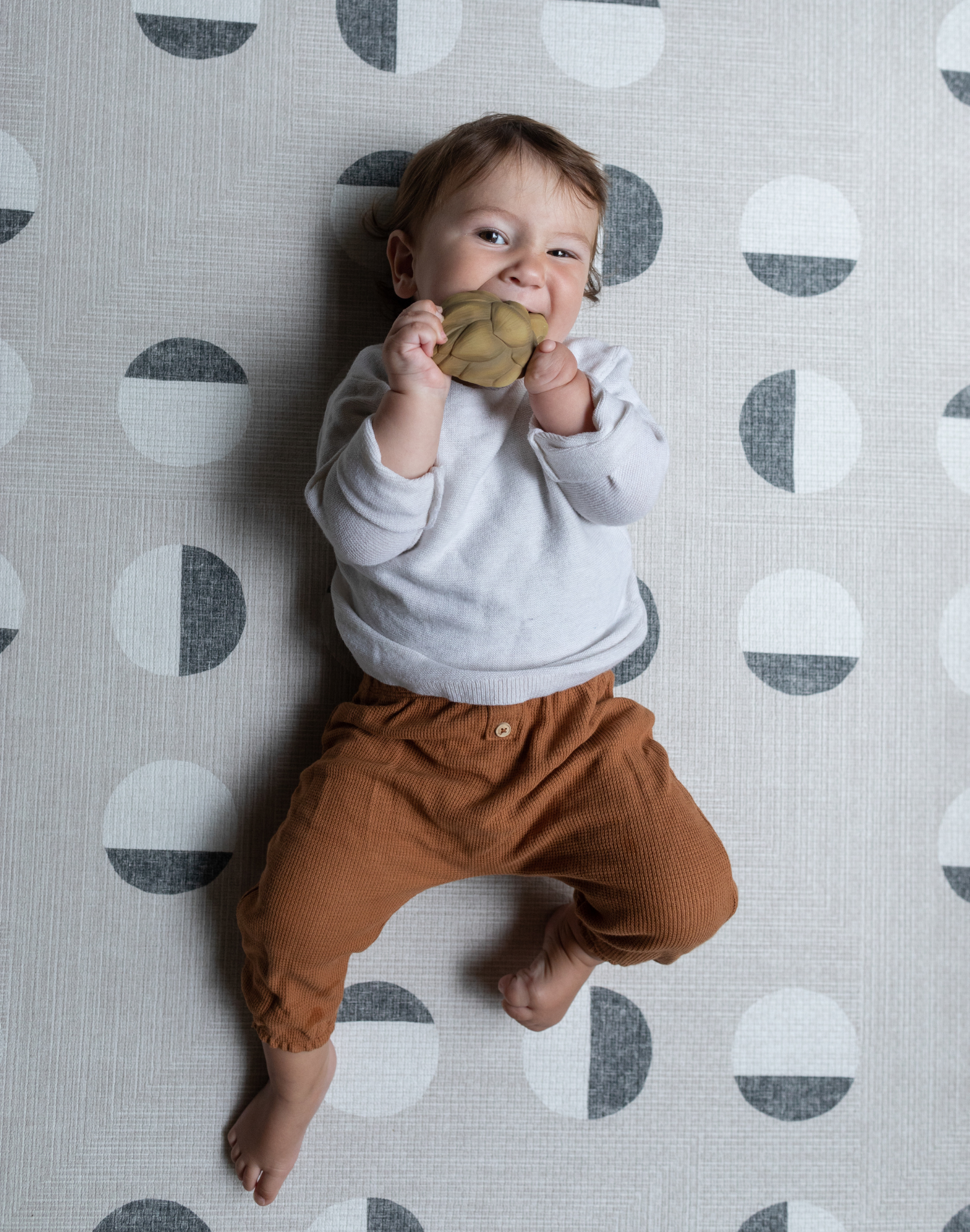 Baby chews on a teether and lays on textured baby play mat that provides support for all types of floor play 