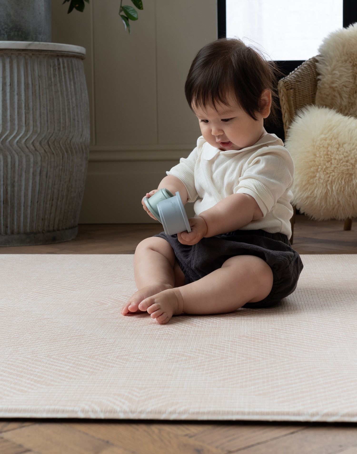 Little girl plays with stacking cups on comfortable soft playmat 