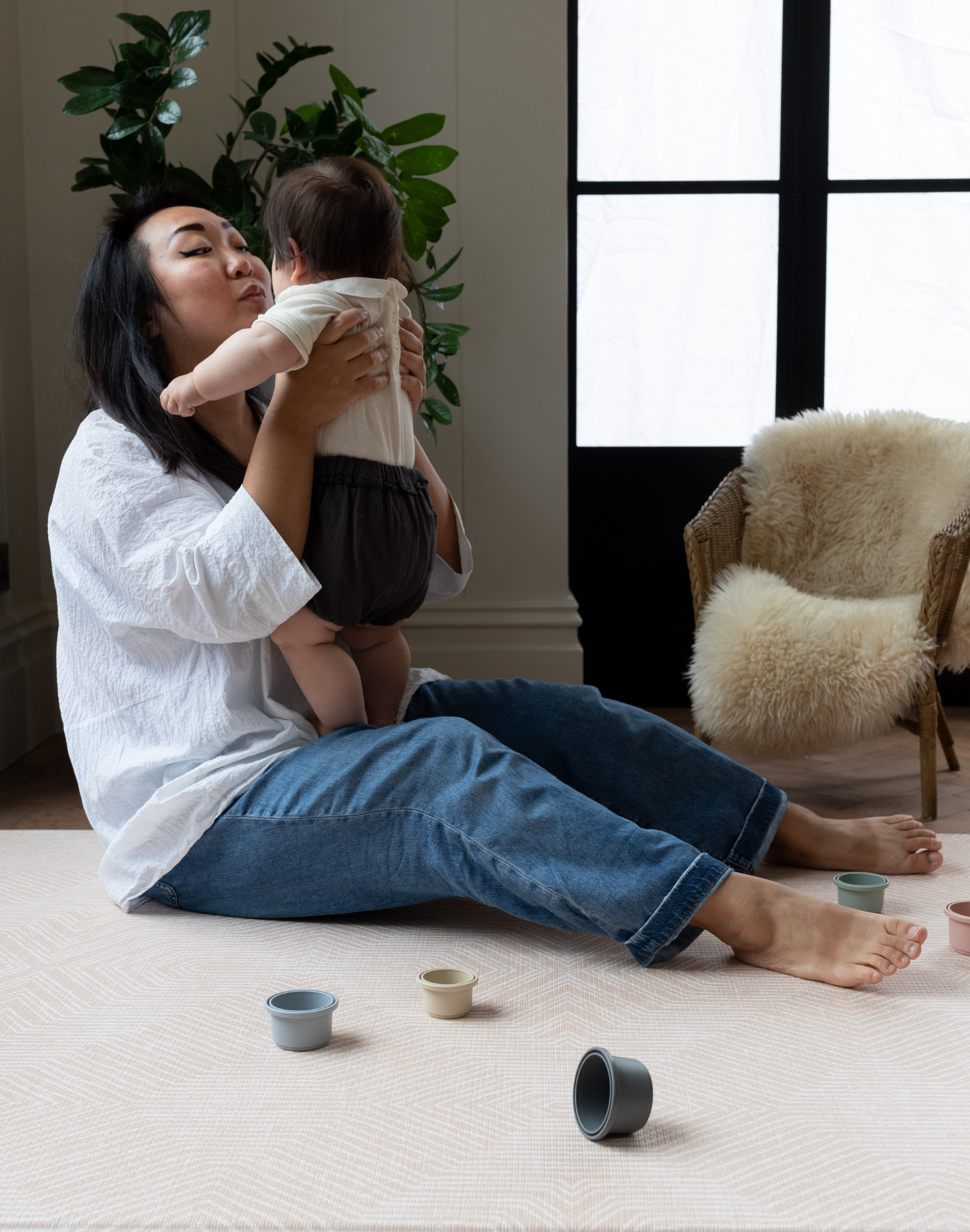 Lady holds baby and sits comfortably on soft baby playmat designed for the whole family 