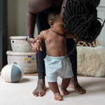 Mother kisses little boy on the light pink playmat with neutral kilim pattern 