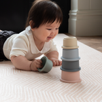 Baby stacks mushie cups on millenial pink playmat designed to look subtle in the home