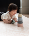 Baby stacks mushie cups on millenial pink playmat designed to look subtle in the home